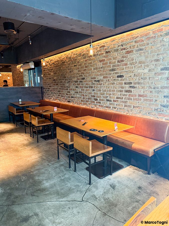 Interno del locale a Kinka Sushi Bar Izakaya a Shibuya con tavoli in legno, panche in pelle e parete in mattoni.