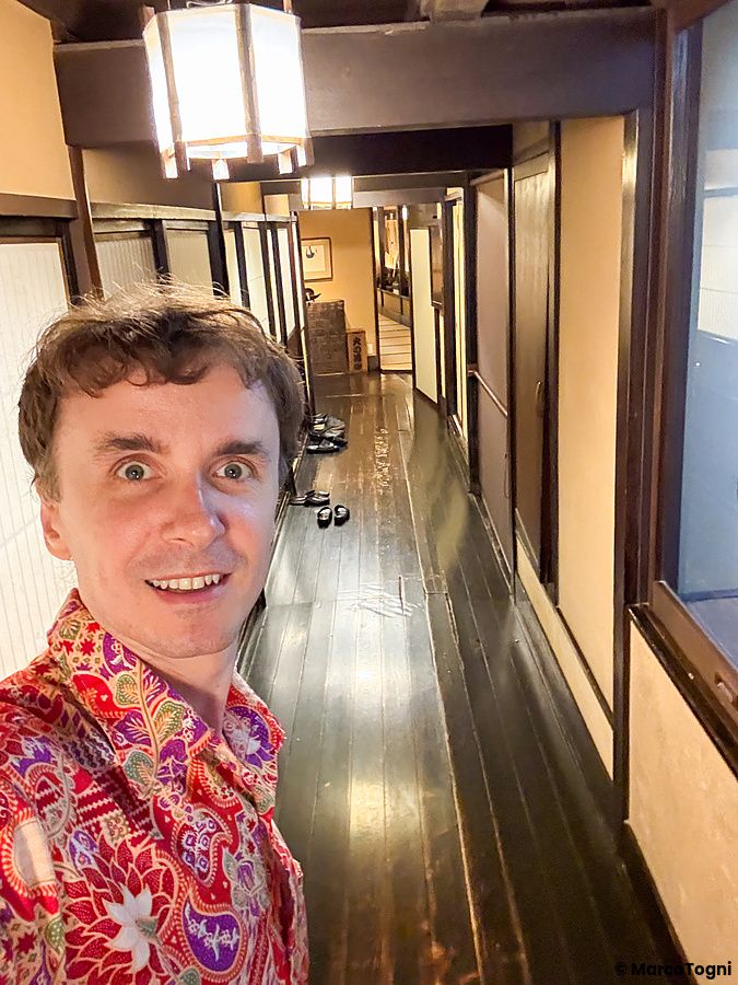 Marco Togni sorridente si scatta un selfie all'interno del ristorante a Kurochaya, lungo un corridoio in legno scuro.