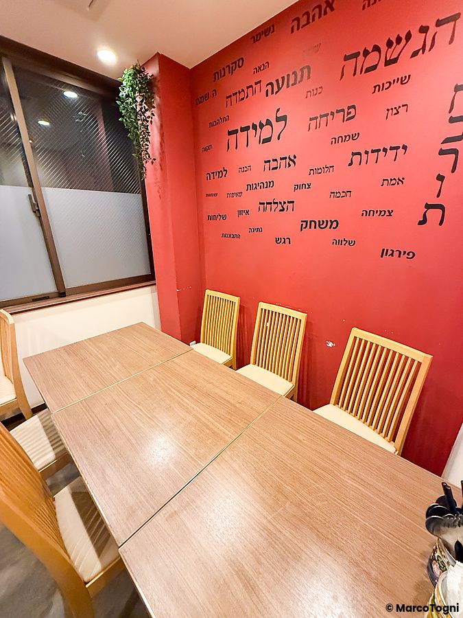 Vista interna del Ristorante Telaviv a Kyoto con un tavolo in legno davanti a una parete rossa decorata con scritte.