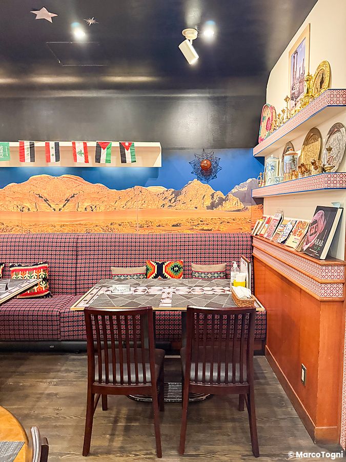 Interno a Seven Hills, un ristorante arabo a Osaka con divanetto a quadri, tavoli e un murale del deserto sulla parete.