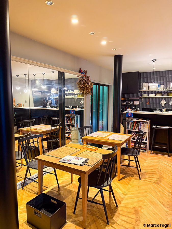 Veduta dell'interno a VeganLife SoiSoi a Kyoto, con tavoli in legno, sedie nere, cucina a vista e pavimento in parquet.