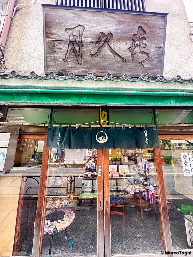 Facciata della storica pasticceria Kikuzuki a Yanaka con tenda noren verde e insegna in legno sopra l'ingresso.