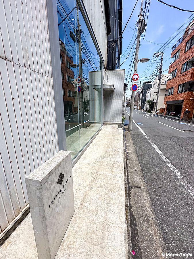 L'ingresso moderno del Koffee Mameya Kakeru a Tokyo con un'insegna in cemento sul marciapiede accanto a una strada.