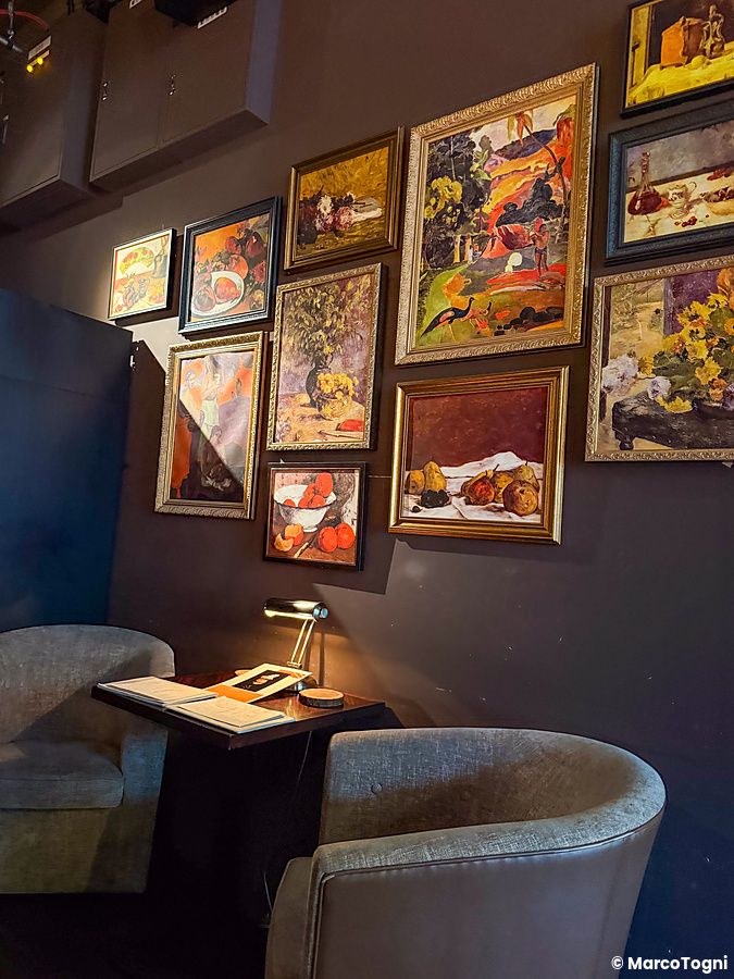 Interno del bar Memento Mori a Tokyo con una parete decorata da numerosi quadri incorniciati sopra un tavolino.