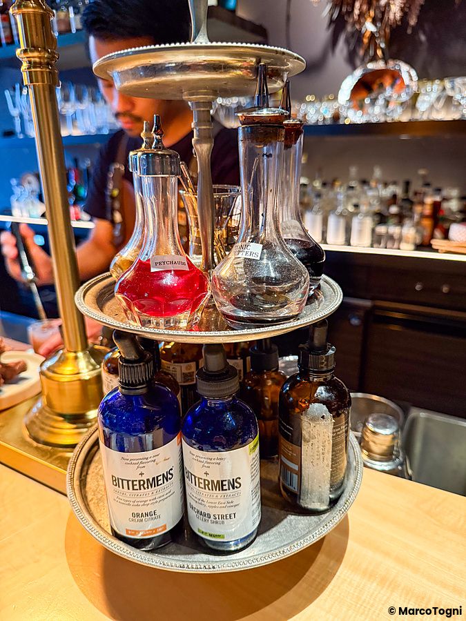 Un espositore a due ripiani con boccette di bitter sopra il bancone del bar Memento Mori a Tokyo.