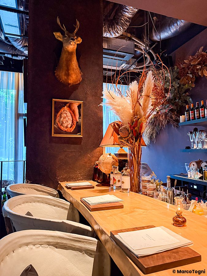 Interno del bar Memento Mori a Tokyo con bancone in legno, decorazioni floreali secche e una testa di cervo a parete.