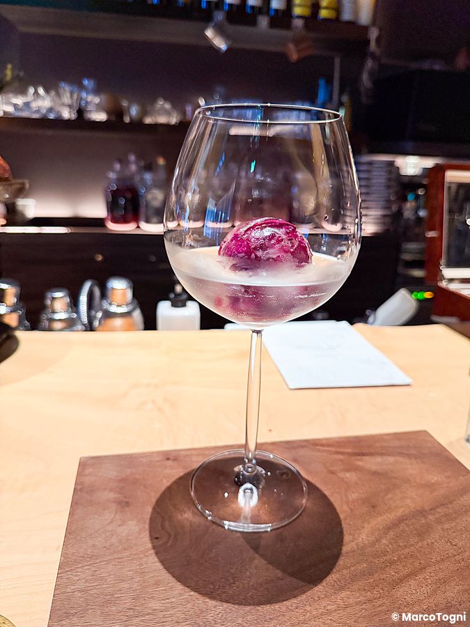 Un calice con un cocktail e una sfera di ghiaccio colorata sul bancone in legno del bar Memento Mori a Tokyo.