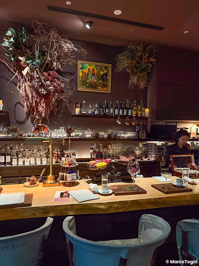 Il bancone del bar Memento Mori a Tokyo con drink, decorazioni floreali essiccate e un individuo che lavora dietro.