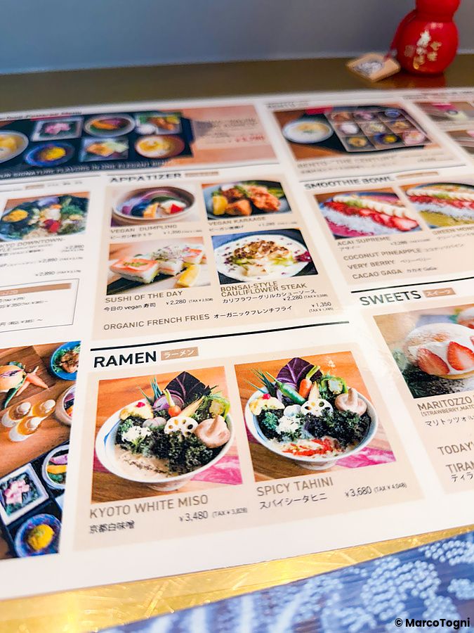 Menù illustrato con piatti vegani, tra cui ramen e sushi, poggiato su un tavolo del Tokyo Vegan Ramen Center a Harajuku.