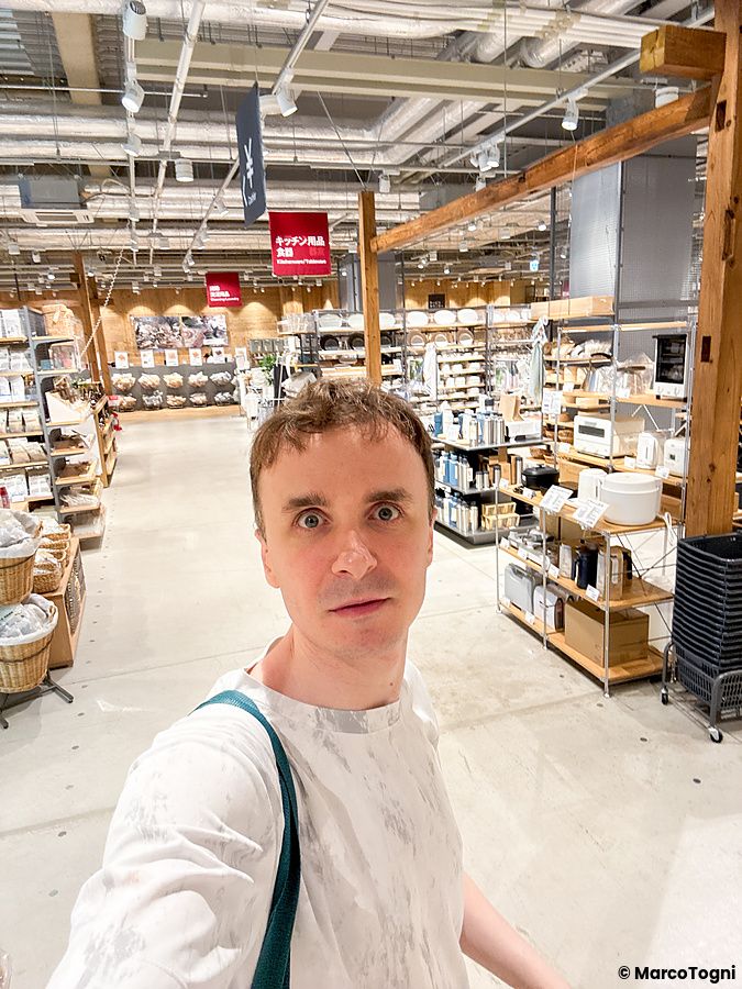 Marco Togni scatta un selfie all'interno del negozio Muji a Tokyo, circondato da scaffalature piene di prodotti per la casa.