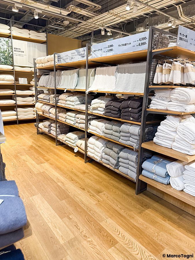 Scaffalature in metallo e legno piene di biancheria da letto ordinata all'interno del negozio Muji, a Tokyo.