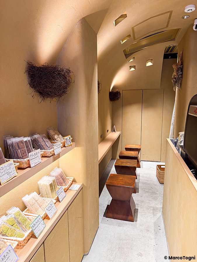 Interno della pasticceria vegana Naki vegan sweets a Namba, Osaka, con scaffali di dolci e sgabelli in legno.