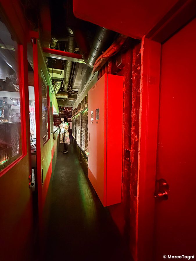 Uno stretto corridoio all'interno a Neo Shinjuku Atsushi, caratterizzato da pareti rosse e una persona in fondo.