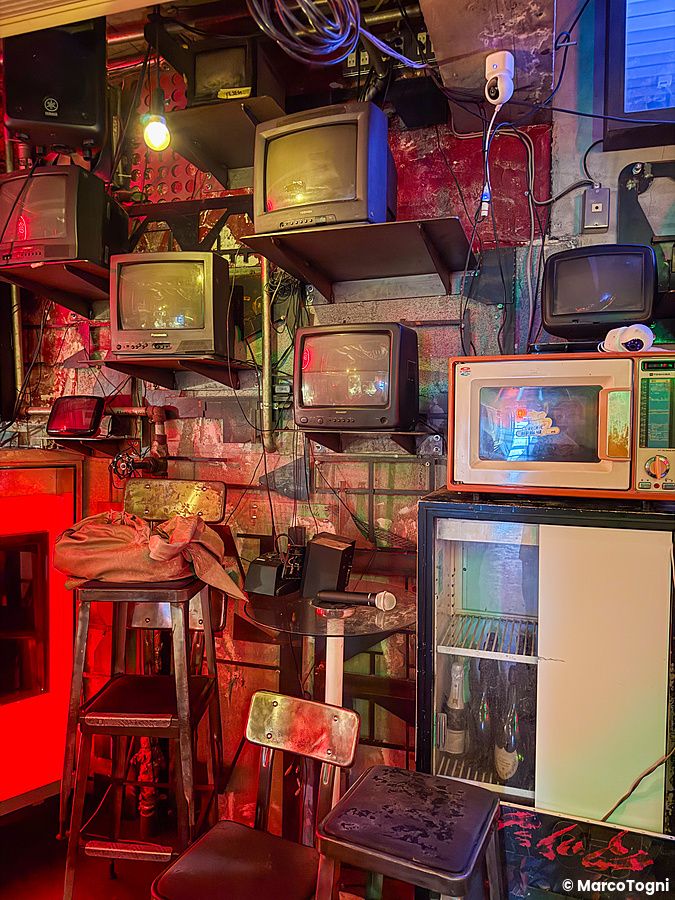 Una parete all'interno a Neo Shinjuku Atsushi decorata con schermi a tubo catodico e arredamento in stile industriale.