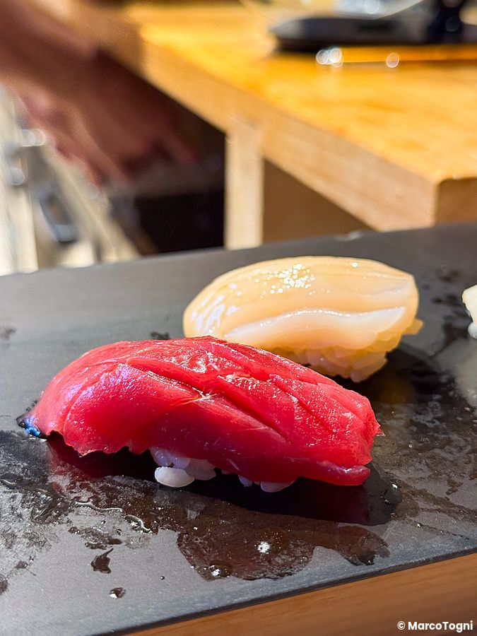 Un nigiri di tonno a Sushi & Bar Fujiro Marunouchi Tokyo servito su un piatto scuro accanto a un altro nigiri.