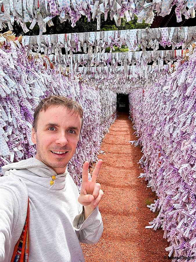 Marco Togni con segno di pace davanti a omikuji al santuario hirosakainari a kanazawa.