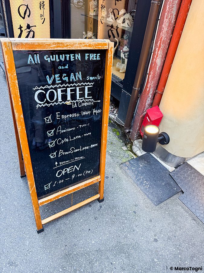 Una lavagna in legno con menu di bevande e scritte vegane davanti all'ingresso di Naki vegan sweets a Osaka.