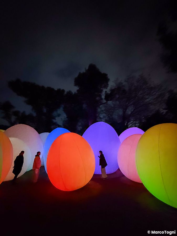 Persone camminano tra grandi uova illuminate da colori vivaci al teamLab Botanical Garden Osaka.
