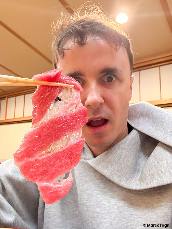 Marco Togni tiene con le bacchette un pezzo di otoro davanti al viso all'interno del ristorante Waunn ad Asakusa.