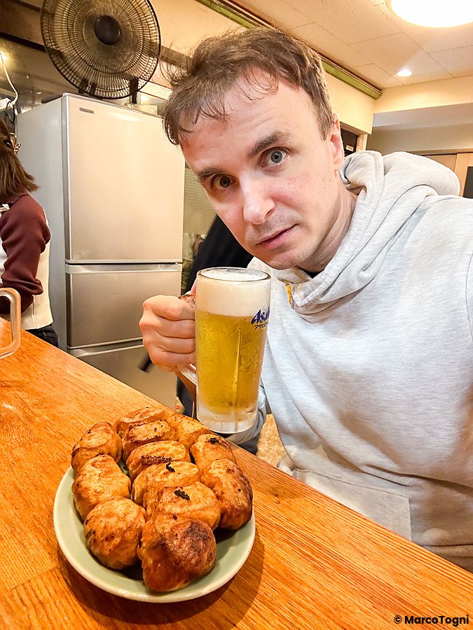 Marco Togni al bancone del ristorante Fight Gyoza a Otsuka con davanti un piatto di gyoza e un boccale di birra Asahi.