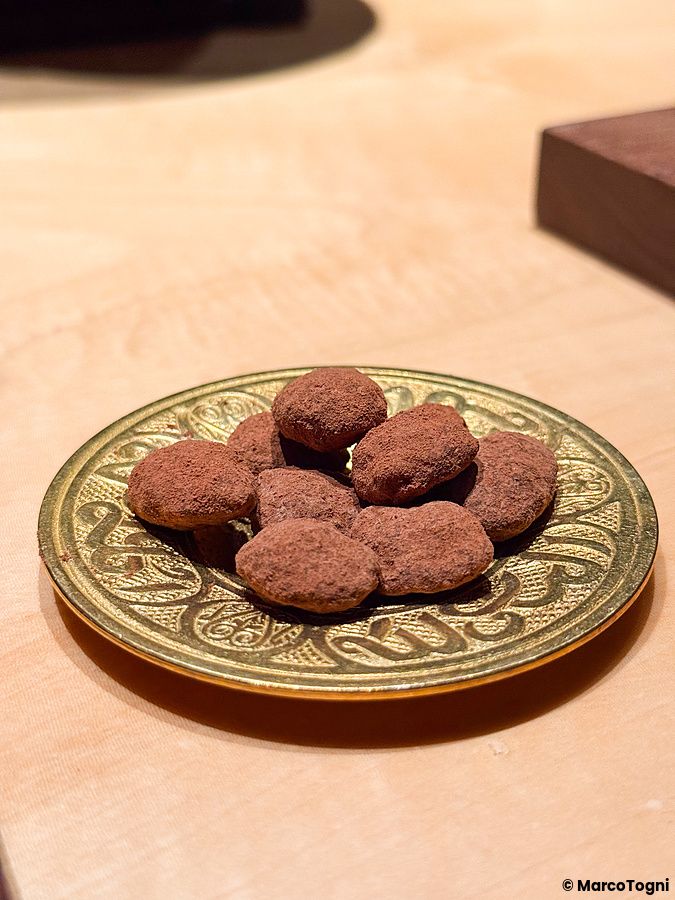 Alcuni tartufi al cacao sono disposti su un piccolo piatto dorato con incisioni su un bancone di legno presso Memento Mori.