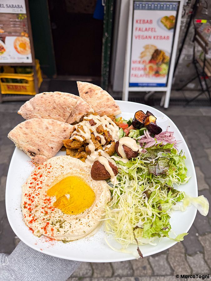 Un piatto misto vegano a Falafel Sababa composto da hummus, falafel, insalata e pane pita tenuto in mano a Namba, Osaka.