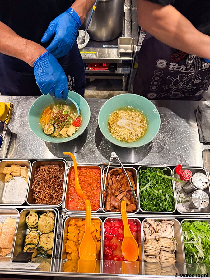 Due persone preparano il ramen vegano a Soranoiro, Ginza, disponendo verdure e ingredienti freschi in ciotole.