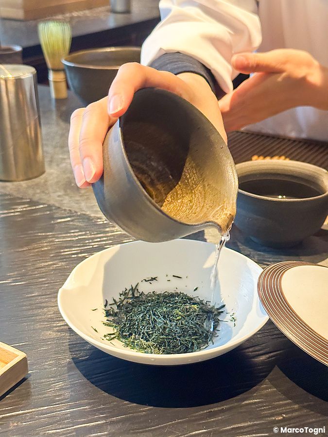 Una persona versa acqua da un bricco di ceramica su foglie di tè gyokuro in una ciotola a Sakurai Japanese Tea Experience.