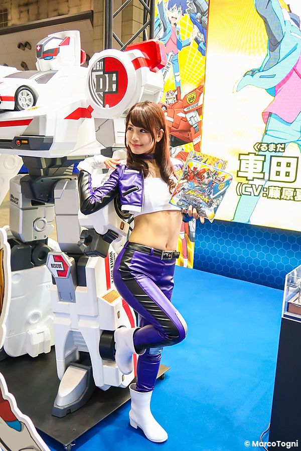 Una promoter in costume viola e bianco posa accanto a una statua di un robot al Tokyo Game Show.