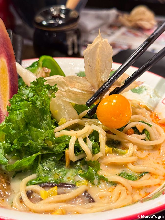 Una bacchetta solleva un frutto di physalis da una ciotola di ramen vegano al Tokyo Vegan Ramen Center.