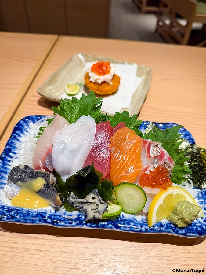 Sashimi assortito e un tortino fritto serviti su piatti di ceramica al Ristorante New Sushi Center Harukiya, Osaka.