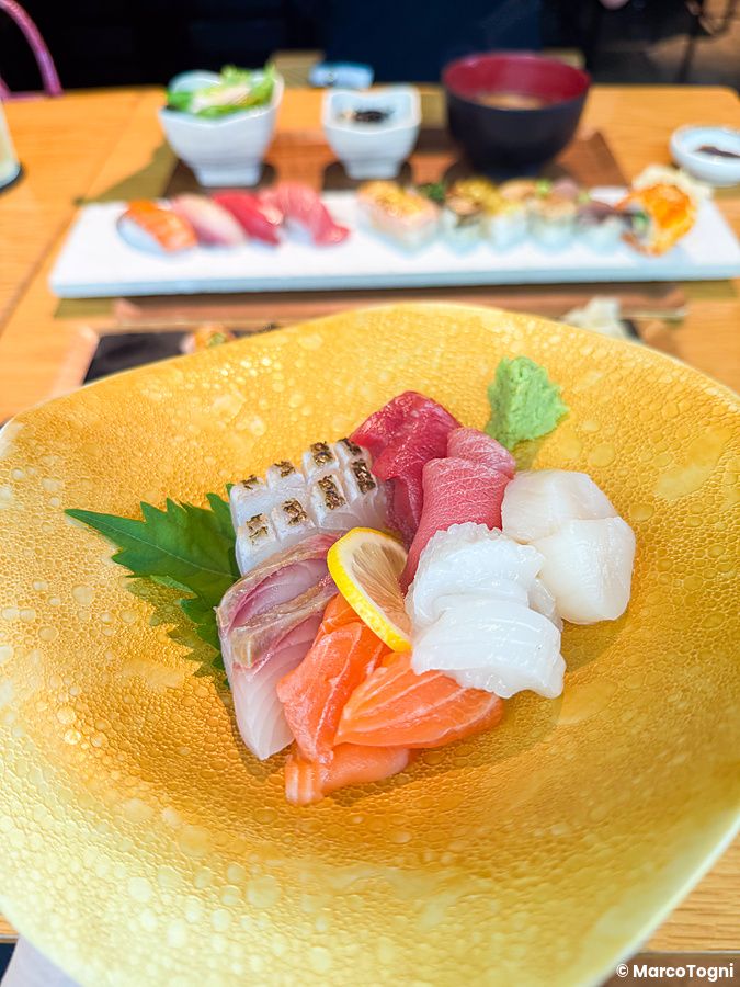 Sashimi misto su piatto giallo testurizzato con sushi e zuppa sullo sfondo presso il Kinka Sushi Bar Izakaya a Shibuya.