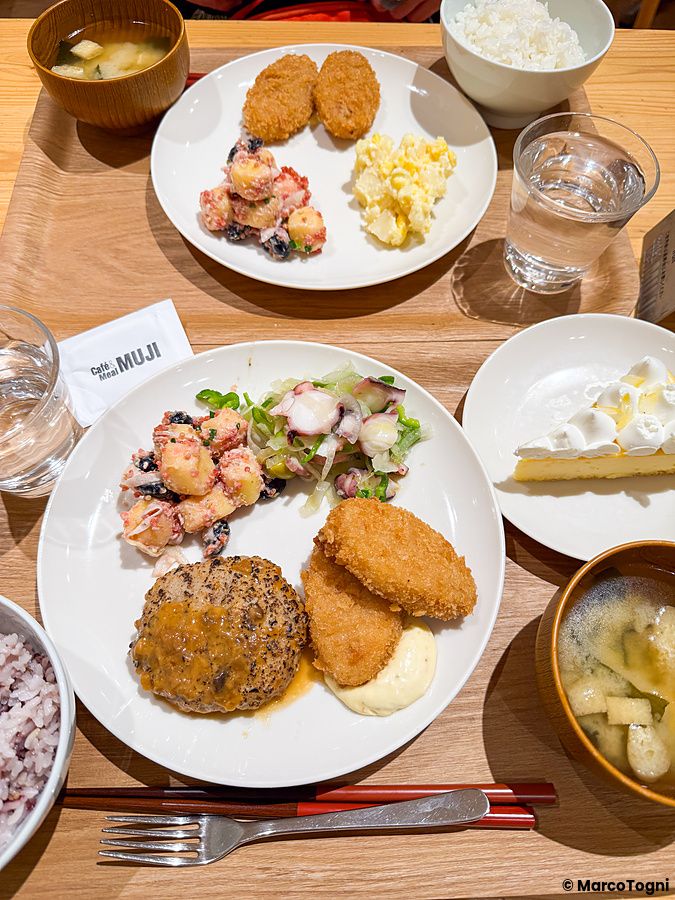 Un set completo a Cafe＆Meal Muji con vari piatti, riso, zuppa di miso e una fetta di torta su un tavolo in legno.