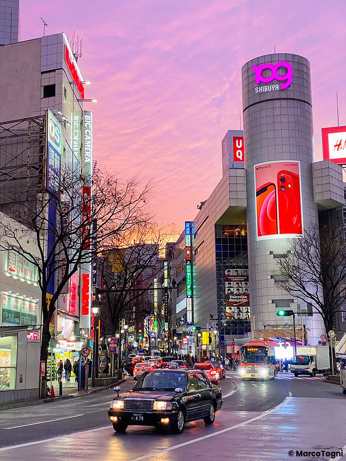 Strada a Shibuya con traffico sotto un cielo rosa al tramonto.