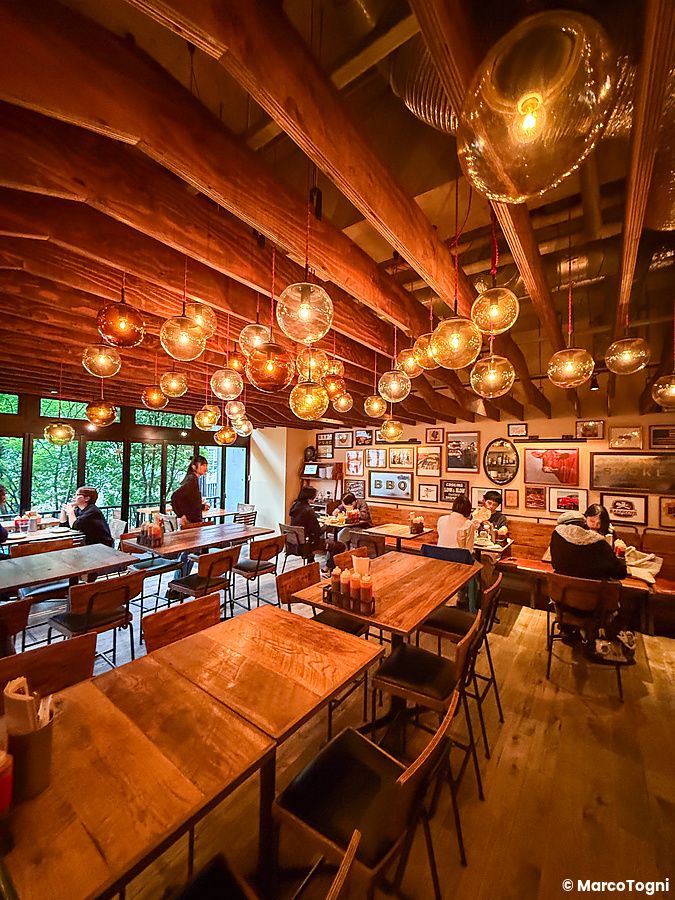 Interno del ristorante Smokehouse a Tokyo con tavoli in legno, travi a vista e persone sedute a mangiare.