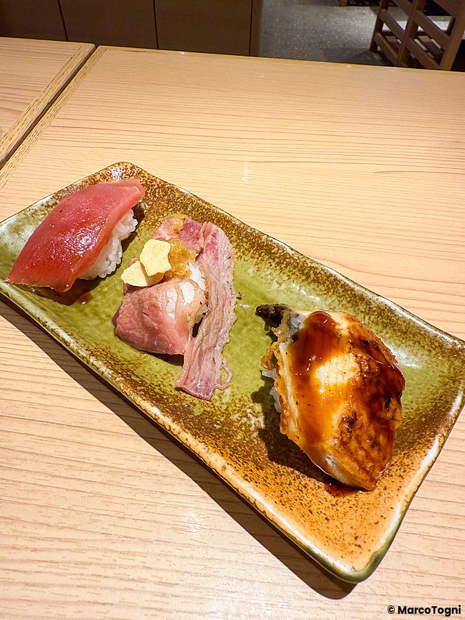 Tre pezzi di sushi vari su un piatto rettangolare in ceramica al Ristorante New Sushi Center Harukiya di Osaka.