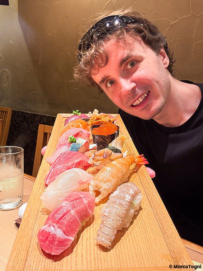 Marco Togni sorridente con un piatto di sushi in un ristorante.