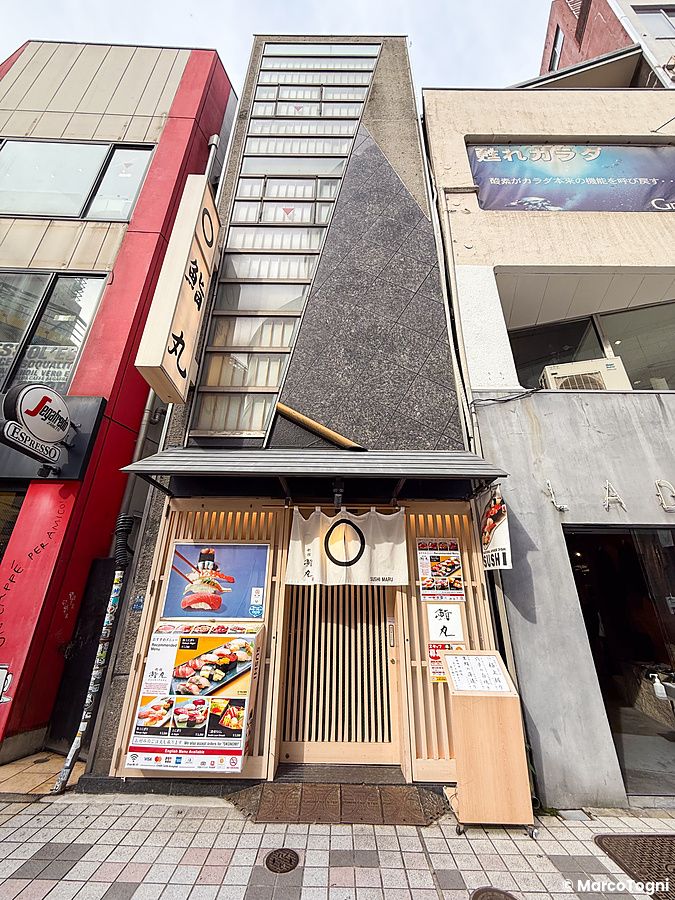 Esterno a Sushimaru, ristorante di sushi a Shinjuku con insegna, porta in legno, tende noren e menu esposti.