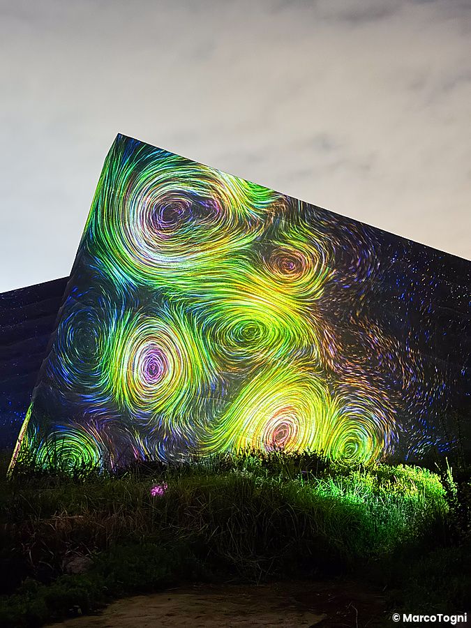 Installazione luminosa con vortici colorati proiettata su una struttura geometrica al teamLab Botanical Garden Osaka.