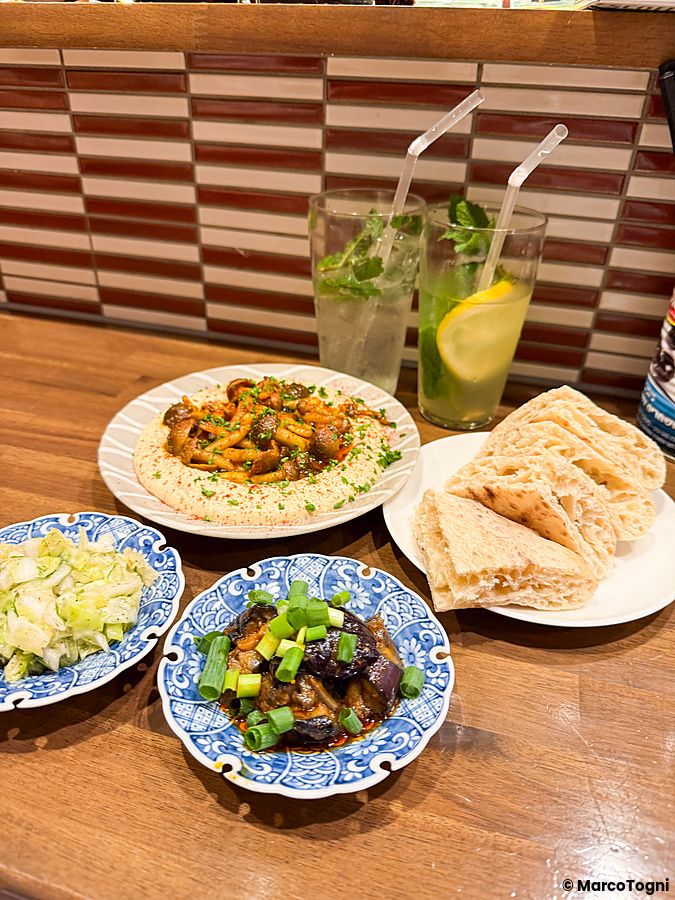 Una tavola imbandita con piatti di hummus, melanzane, pita e bevande presso il ristorante Telaviv a Kyoto.