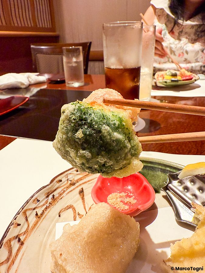 Un pezzo di broccoli in tempura tenuto da bacchette presso il ristorante Ume no Hana a Ginza.