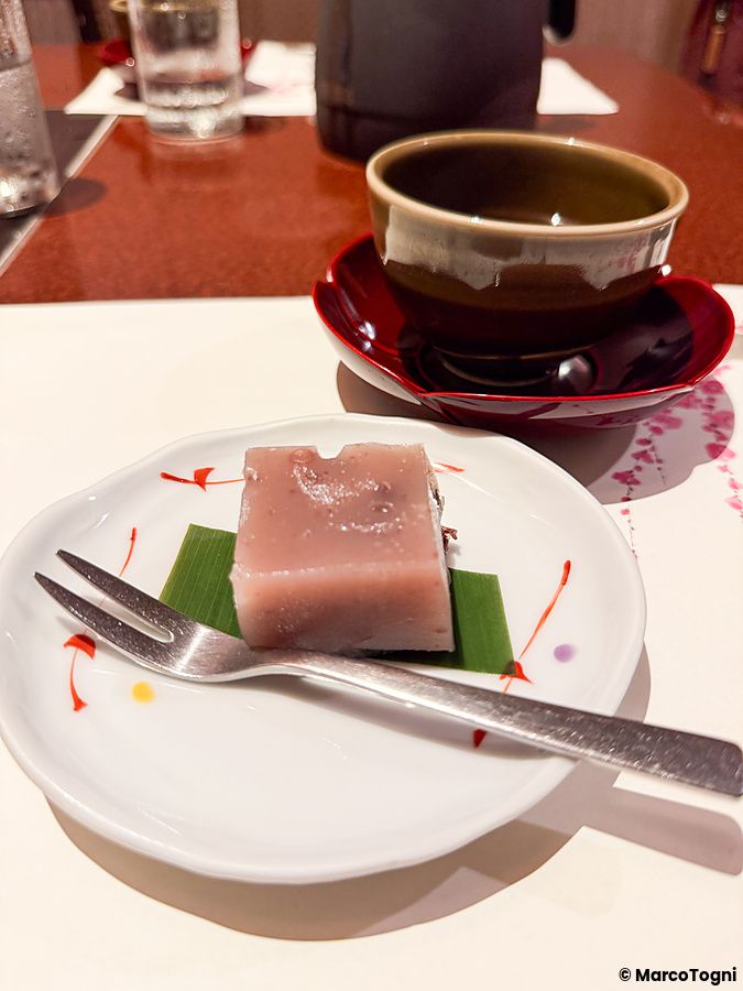 Un cubetto di tofu dolce ai fagioli rossi Azuki servito su un piattino bianco con una forchettina a Ume no Hana.