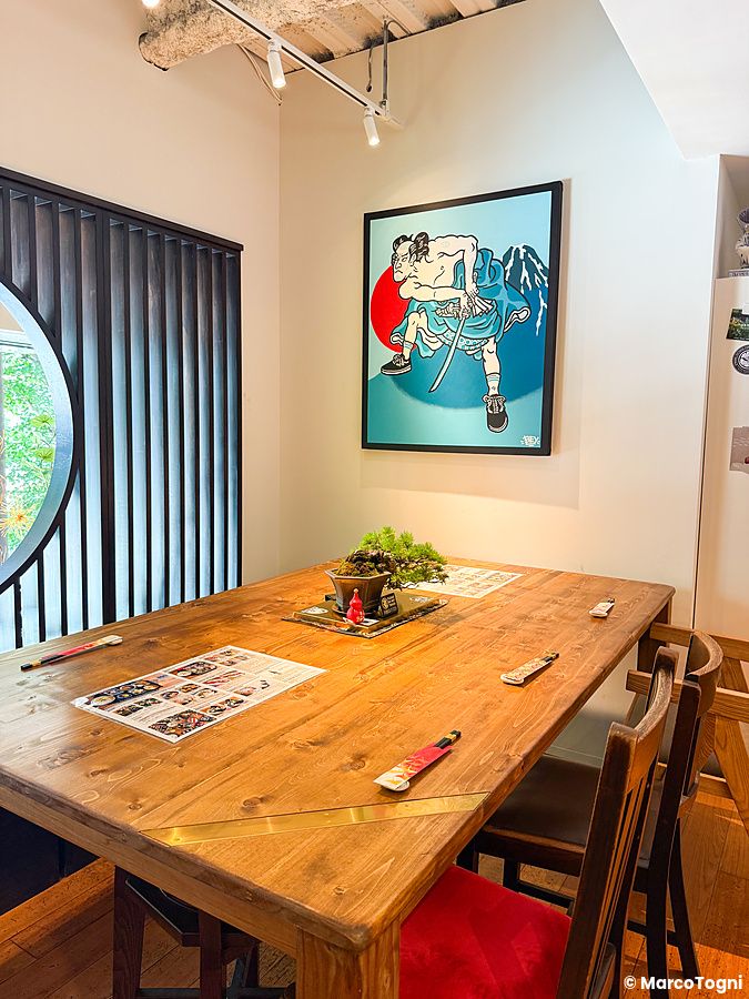 Interno del Tokyo Vegan Ramen Center a Harajuku con un grande tavolo in legno, sedie e un quadro di un samurai.