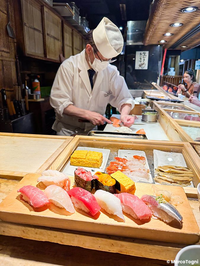 Uno chef prepara il pesce dietro il bancone presso il ristorante Tsukiji Itadori Bekkan, con nigiri sushi in primo piano.