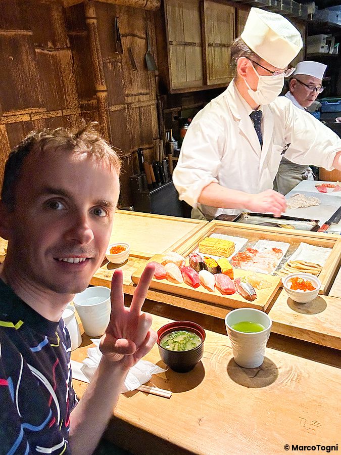 Marco Togni fa il segno di vittoria davanti a un bancone di sushi al ristorante Tsukiji Itadori Bekkan a Tokyo.