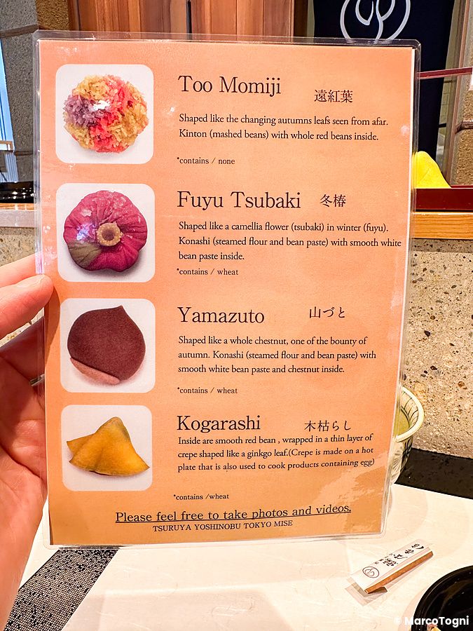 Un menu illustrato di wagashi a Tsuruya Yoshinobu tenuto in mano mostra quattro tipi di dolci tradizionali con descrizioni.