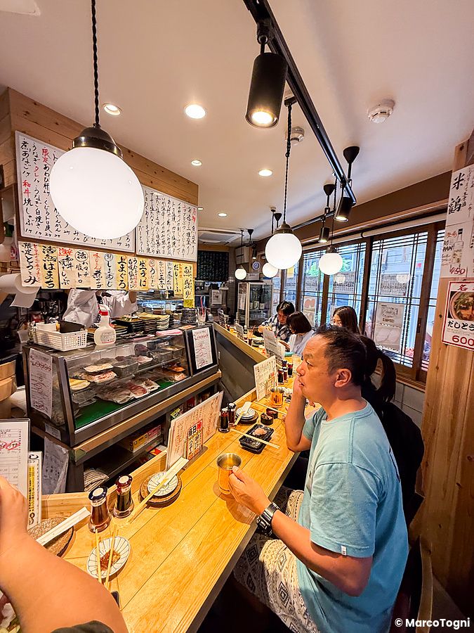 Interno del Ristorante New Sushi Center Harukiya a Ura-Namba, Osaka, con persone sedute al bancone in legno.