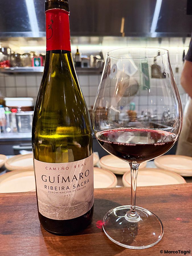 Una bottiglia di vino Guímaro e un calice di vino rosso su un bancone di legno presso il ristorante Mushroom Tokyo.