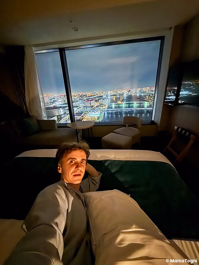 Marco Togni si scatta un selfie a letto presso il Mitsui Garden Hotel Toyosu Premier con vista sulla baia di Tokyo.