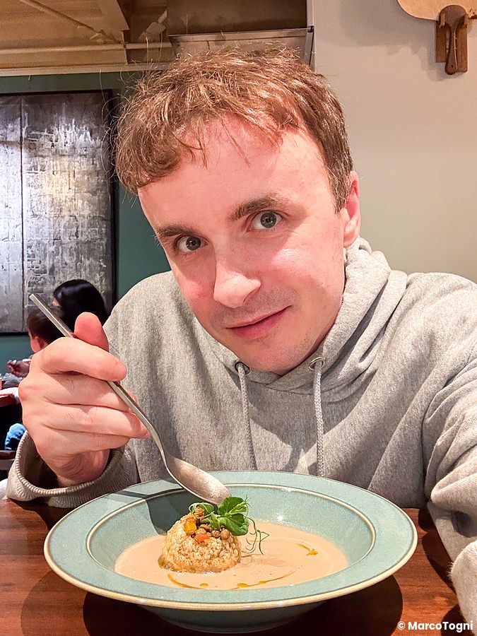 Marco Togni siede a un tavolo presso Mushroom Tokyo a Omotesando mentre mangia una zuppa di funghi con panipuri e lenticchie.